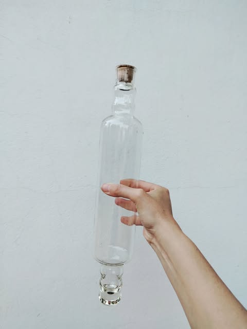 A clear glass rolling pin with a metal cap, held in a hand